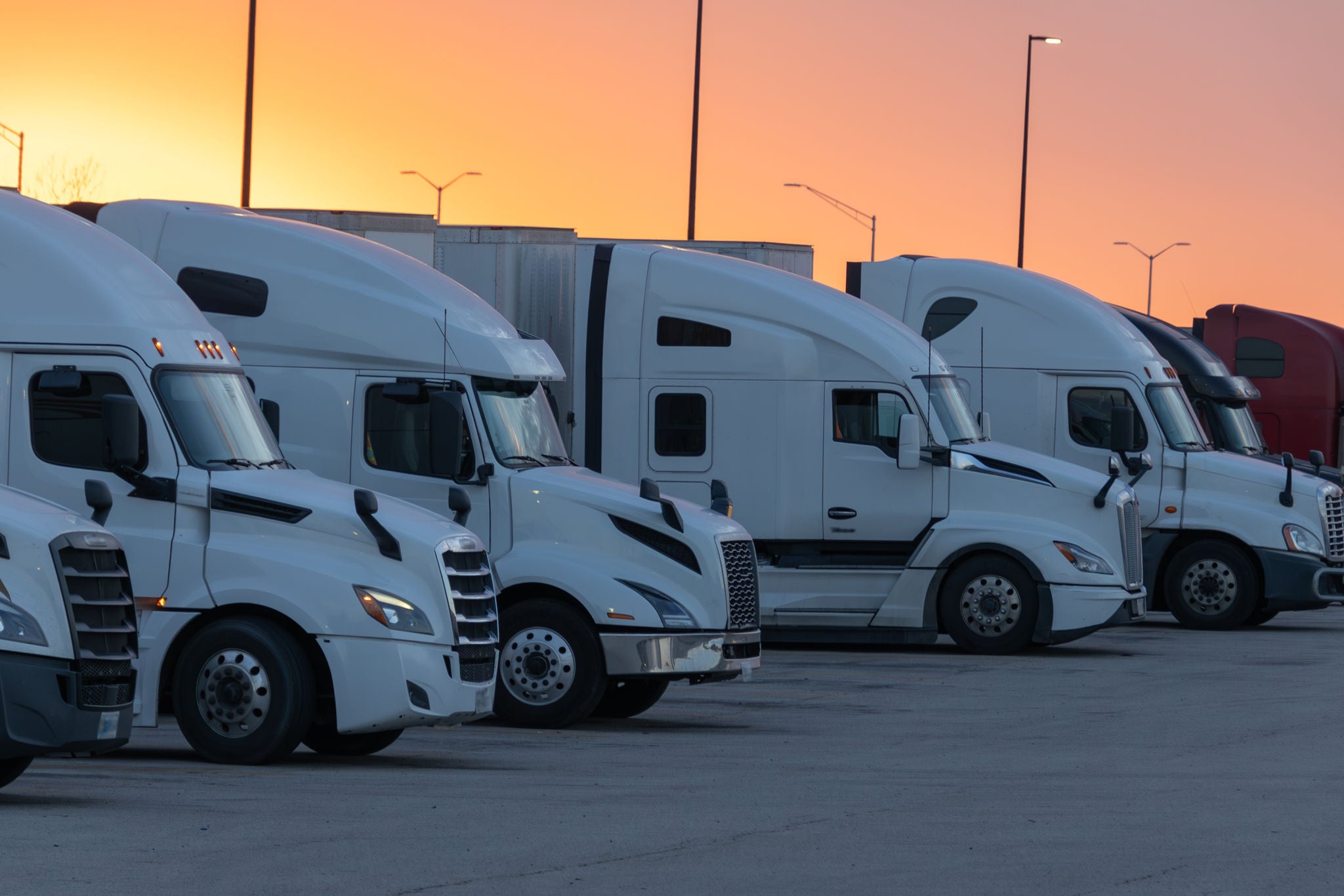 Fleet of trucks parked at dusk with the sunset painting the sky, symbolizing rest after long hauls.