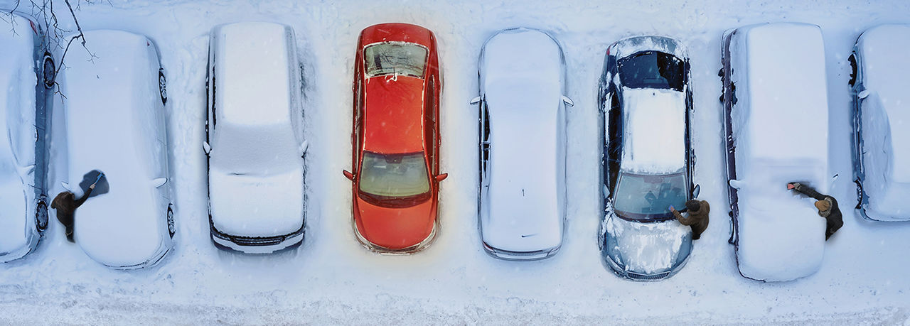 Several cars in parking lot covered in snow and one red car free from snow